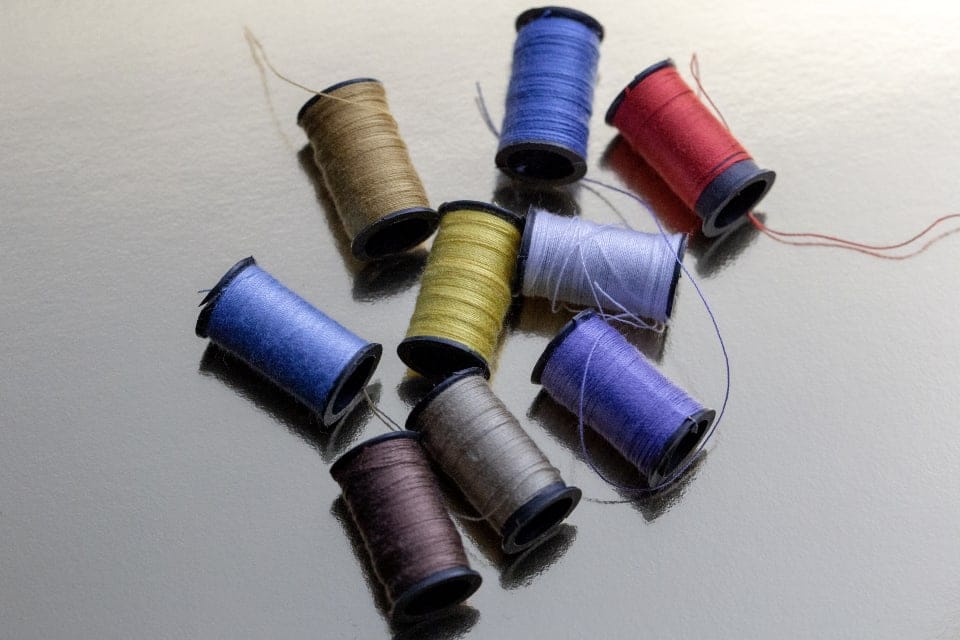 Scattered spools of olive, blue, red and brown thread on steel
