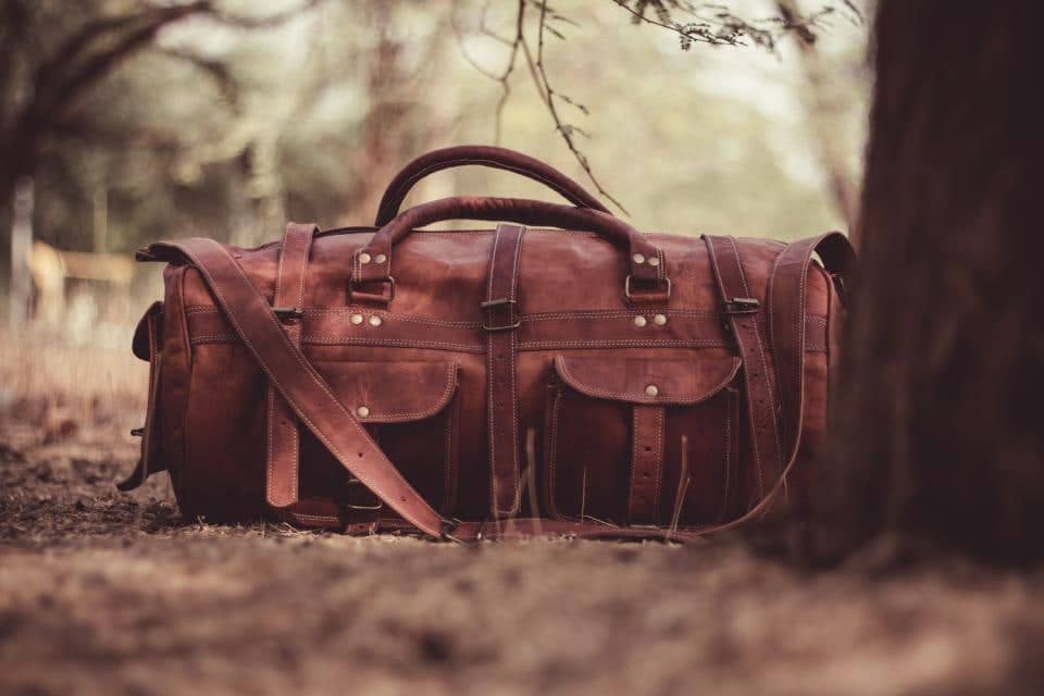 Stitched brown leather duffle bag resting outdoors