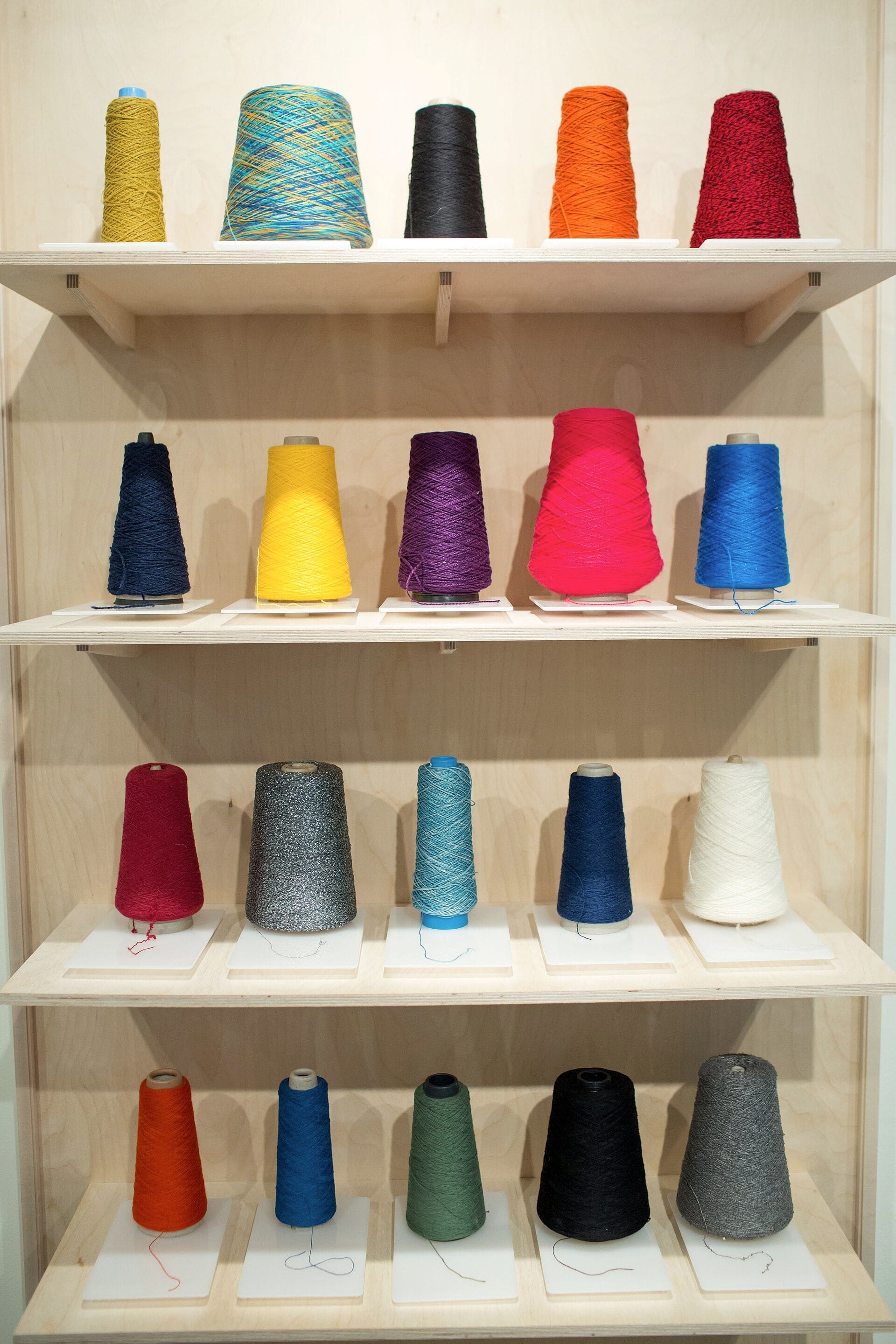 Cones of navy, yellow, purple, pink, blue, red, grey, teal and white yarn on shelves