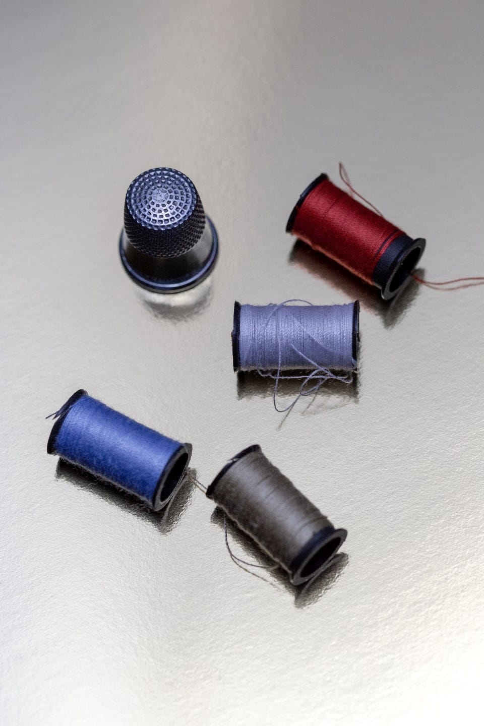 Spools of blue and charcoal thread on a reflective steel surface