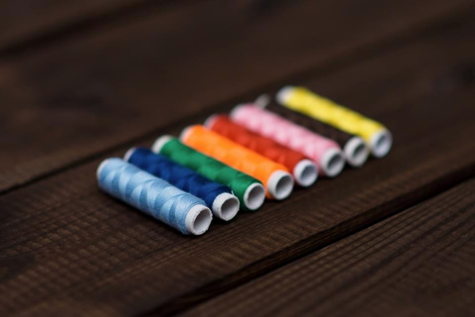 A diagonal row of colourful thread spools on dark wood