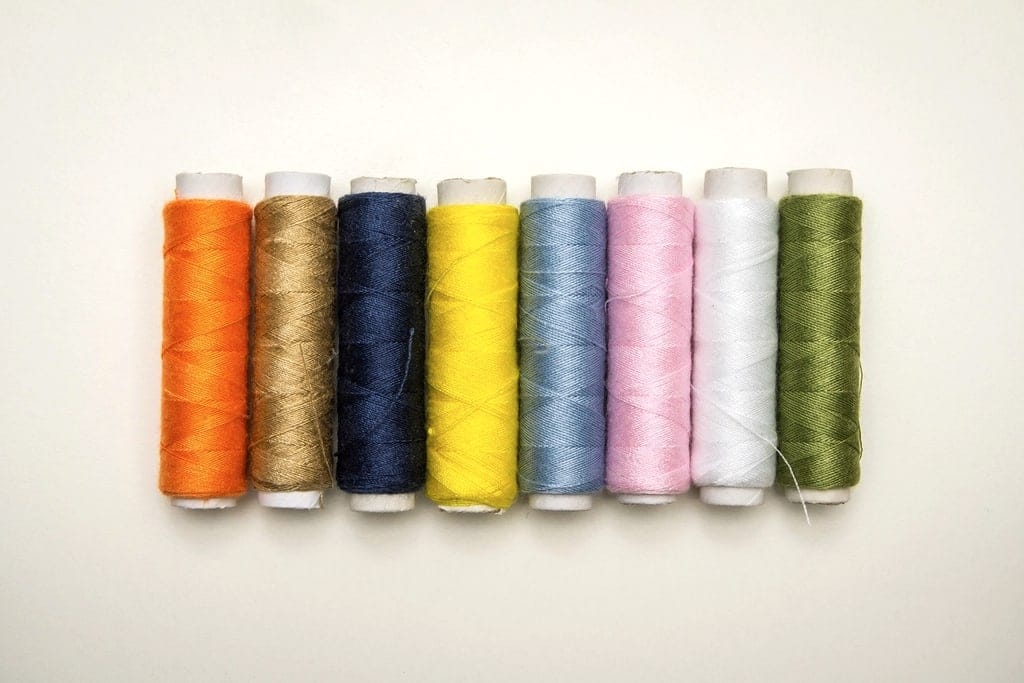 A row of polyester sewing thread spools in orange, gold, navy, yellow, blue, pink, white and olive